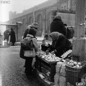 Dorośli i dzieci robią zakupy w drodze ze szkoły. Stoisko przy Hali Mirowskiej, Warszawa, grudzień 1974 r.