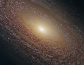 Galaktyka spiralna NGC 2841. Znajduje się w Wielkiej Niedźwiedzicy w odległości 46 milionów lat świetlnych od nas. W środku masywna czarna dziura. Wokół centrum gwiazdy stare. Niebieskie punkty w ramionach to skupiska gwiazd młodych, różowe  to mgławice.