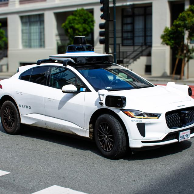 Waymo Jaguar I-PACE wyposażony w technologię samodzielnej jazdy pokonuje skrzyżowanie miasta, widoczne czujniki i kamery.