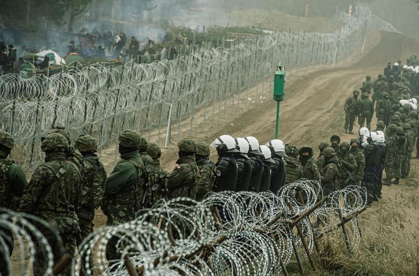 Polscy żołnierze i policja oraz migranci po dwóch stronach polsko-białoruskiej granicy w Kuźnicy