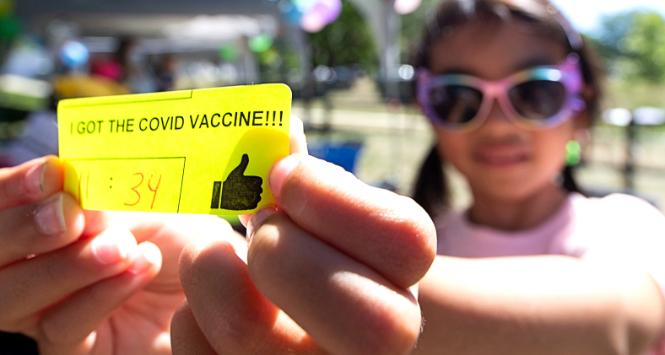 Dziewczynka pokazuje swoją naklejkę po szczepieniu w punkcie szczepień przeciw covid-19 w East Lynn Park w Toronto, Kanada, 12 sierpnia 2022 r.
