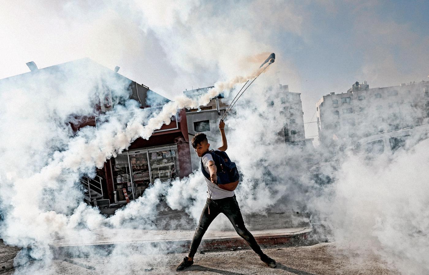 Zamieszki na zachodnim Brzegu, demonstrant odrzuca granat z gazem łzawiącym.