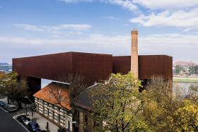 Zaskakująca jest bryła, przypominająca wielką nieregularną bramę, wznoszącą się ponad i jakby otulającą zabytkowy, zrewitalizowany budynek dawnej elektrowni (to nawiązanie do słynnych kantorowskich ambalaży, czyli opakowań).