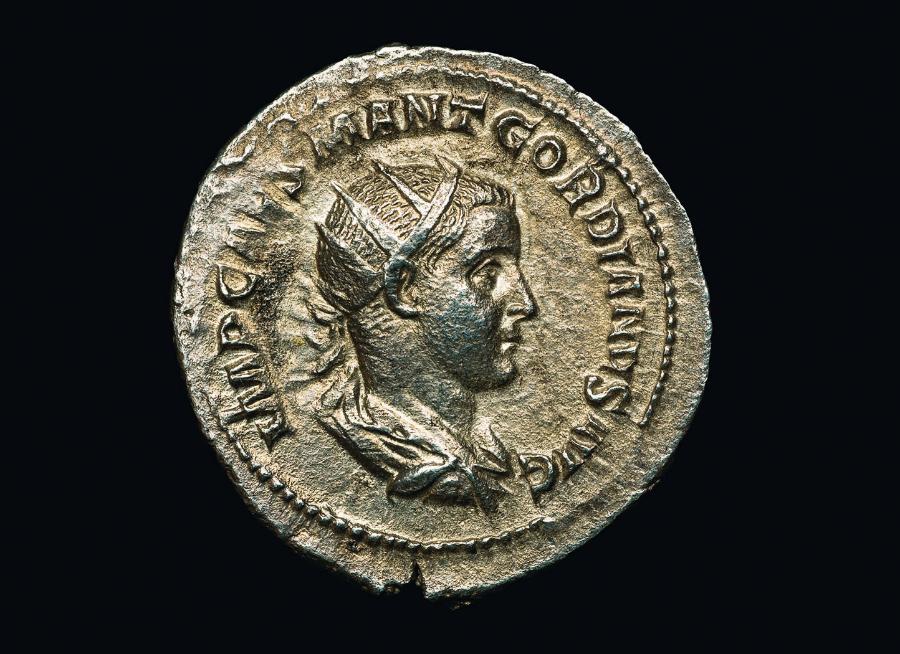 Srebrna macedońska tetradrachma z odwzorowaniem głowy Apollina (V–IV w. p.n.e.), poniżej złote monety Krezusa, króla Lidii (VII w. p.n.e.), obok starożytna rzymska srebrna moneta przedstawiająca imperatora Gordianusa.