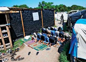 Modlący się imigranci w „bidonville”, miasteczku baraków, w Calais.