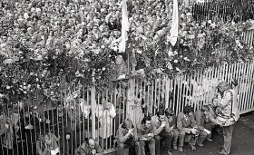 Portret papieża na bramie. Za bramą co dzień nowy tłum. Kwiaty, owoce, żywność to drobne oznaki poparcia dla strajkujących. Nastrój jak podczas pielgrzymki Jana Pawła II rok wcześniej.