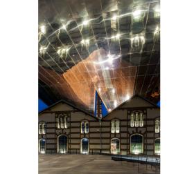 Zaskakująca jest tu już sama bryła, przypominająca wielką nieregularną bramę, wznoszącą się ponad i jakby otulającą zabytkowy, zrewitalizowany budynek dawnej elektrowni.