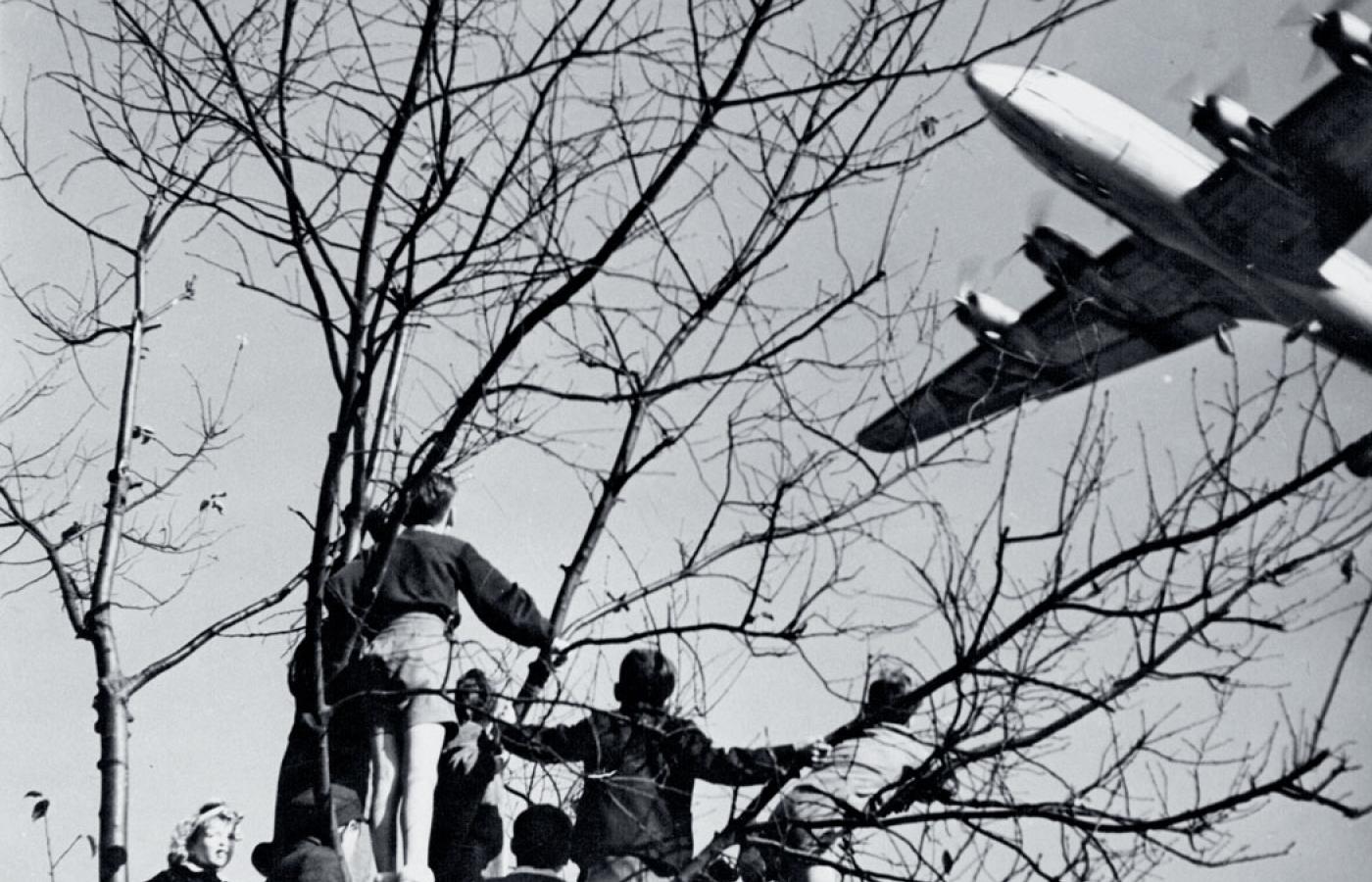 Młodzi berlińczycy oglądają amerykański samolot z pomocą dla zachodnich sektorów miasta podczas zarządzanej przez Stalina blokady Berlina, okolice Bramy Brandenburskiej, czerwiec 1948 r.