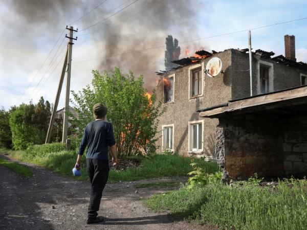 Mieszkaniec stoi w pobliżu płonącego domu, który został trafiony przez rosyjskiego drona w mieście położonym na linii frontu.