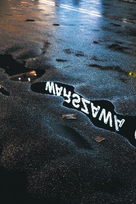 Neon z napisem Warszawa odbijający się w kałuży