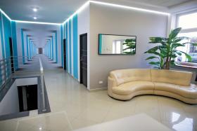 W progu wózek inwalidzki dla klienta w niedyspozycji ruchowej. Jest wieziony nim do poczekalni, gdzie przesiada się na skórzaną sofę.