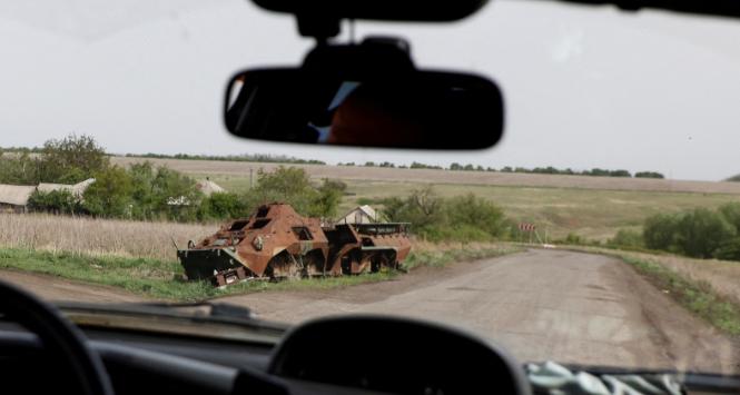 Ukraińscy żołnierze przejeżdżają samochodem obok opuszczonego rosyjskiego transportera opancerzonego w pobliżu linii frontu w obwodzie donieckim. 26 kwietnia 2024 r.