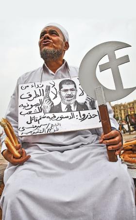 Jeden z protestantów na placu Tahrir. Na szyi zawiesił podobiznę prezydenta Mursiego z napisem „Trucizna konstytucji nas zabije.”