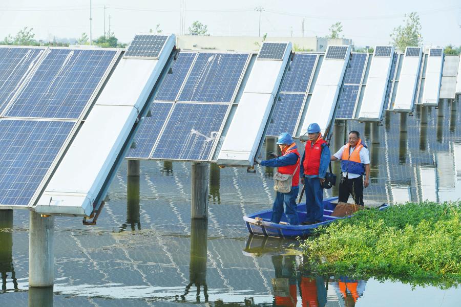 Obsługa elektrow­ni kontroluje panele ustawione na jeziorze w chińskiej prowincji Anhui. W tym samym jeziorze rybacy łowią ryby.