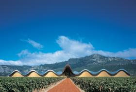 Laguardia (Álava) – winnica YsiosProwincja Álava (graniczy z La Rioja) uchodzi za jeden z najpiękniejszych winnych regionów. Musiała tu więc powstać winnica na miarę oczekiwań. Projekt sporządził Santiago Calatrava, najsłynniejszy współczesny hiszpański architekt. To za jego sprawą wina z etykietą D.O.C. Rioja przeniosły się w XXI wiek i kojarzą z najlepiej rozumianą awangardą. Budynek wtapia się nienachalnie w krajobraz u podnóża gór Kantabryjskich i rzędów winorośli.