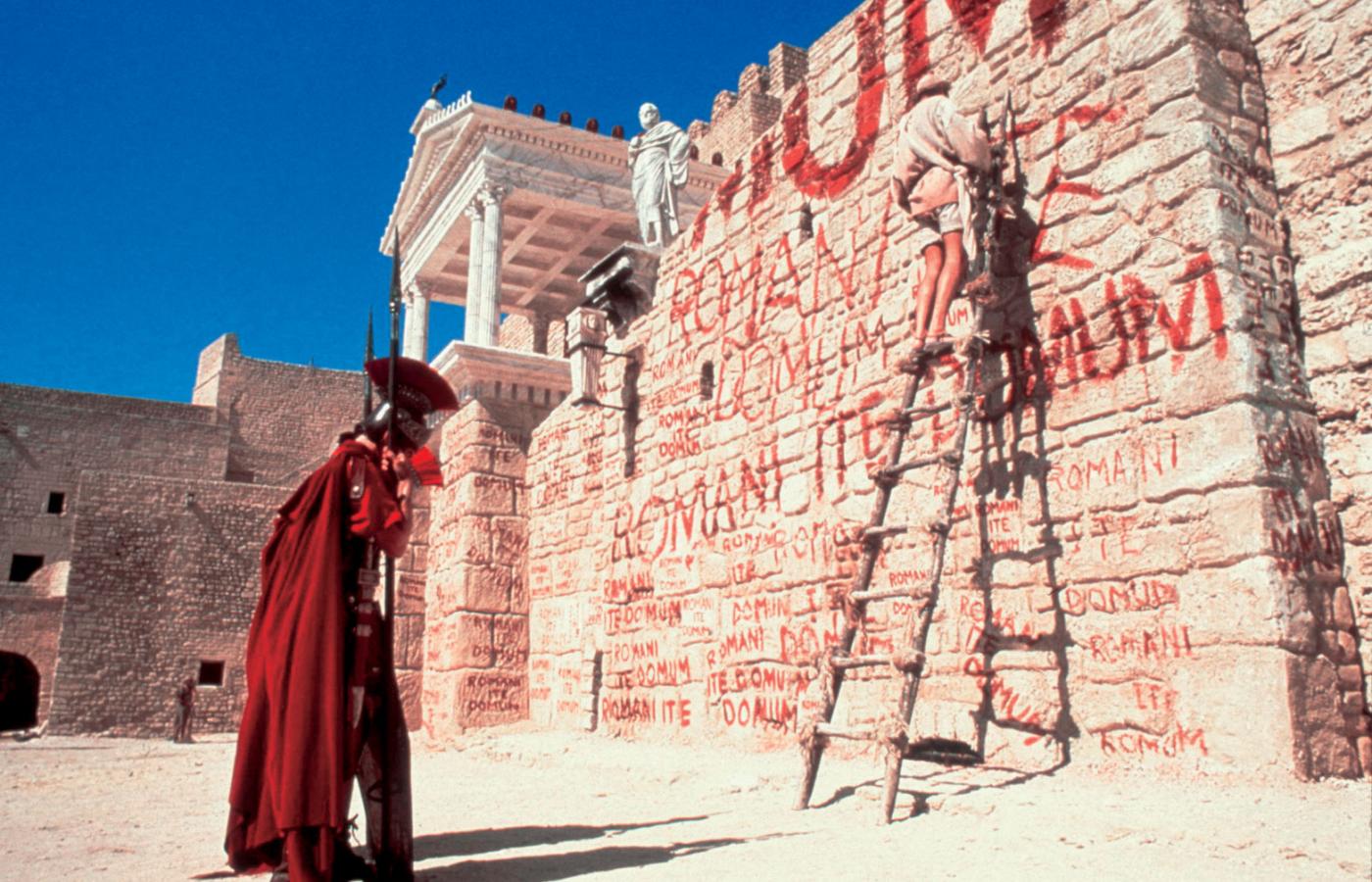 Gramatyka ważniejsza niż polityka? Gdy główny bohater „Żywotu Briana” Monty Pythona pisze nocą na murze świątyni w Jerozolimie „Romanes eunt domus”, chwyta go rzymski centurion i przepytuje, jak poprawnie brzmi hasło „Rzymianie idźcie do domu”, po czym, jak na belfra przystało, każe mu napisać „Romani ite domum” sto razy.