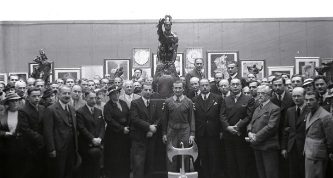 Wystawa prac Stanisława Szukalskiego i „Szczepu Rogate Serce” w gmachu Towarzystwa Przyjaciół Sztuk Pięknych (Pałac Sztuki) w Krakowie, 1936 r. Stanisław Szukalski stoi w środku za hełmem z symbolem Toporła. W tle pośrodku rzeźba „Remussolini” (projekt pomnika Mussoliniego), z lewej rzeźba „Bolesław Prawy (Śmiały)”.