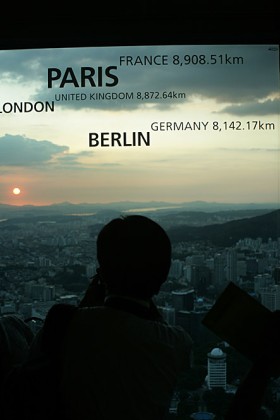 Spojrzenie na zachód  przez szybę kawiarni.  Napisy przypominają turystom, jak daleko są od domu. Powinny też uświadomić,  że siedzący obok Koreańczycy właśnie wysłali do tych miast wyroby swoich korporacji: LG, Samsunga, Hyundaia