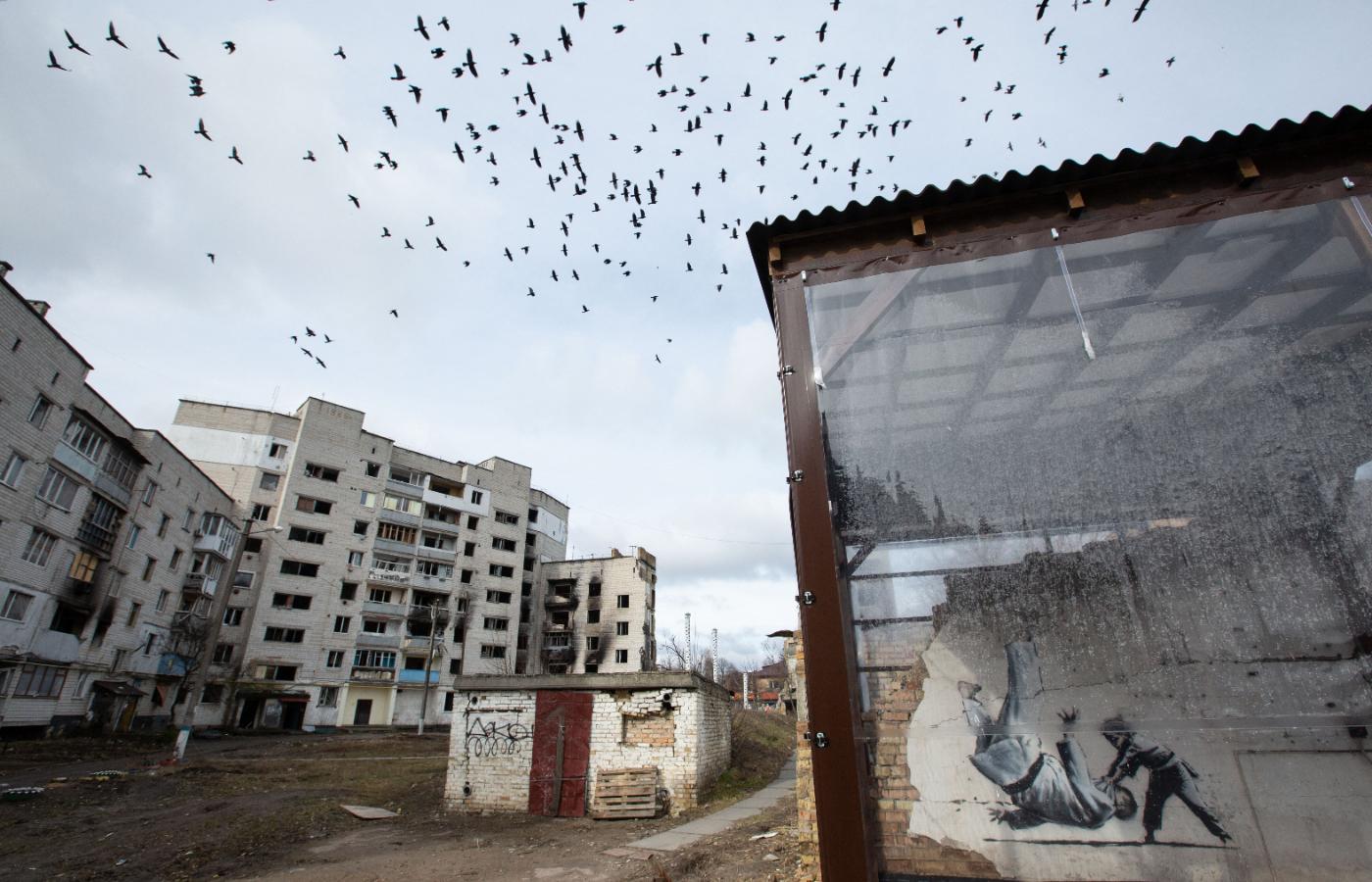Widok zniszczeń w mieście Borodianka i graffiti angielskiego artysty Banksy′ego na jednej ze ścian zniszczonego bloku. 26 lutego 2023 r.