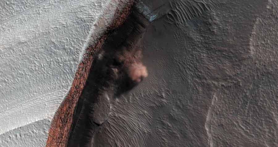 Lawina: Na tym zdjęciu, wykonanym w 2010 roku za pomocą kamery wysokiej rozdzielczości HiRISE, chmura gruzu unosi się nad miejscem w pobliżu bieguna północnego Marsa. Najprawdopodobniej są to skutki lawiny. Widać strome urwisko z warstw wodnego lodu pokrytego jasnym, białym szronem z dwutlenku węgla. W każdą marsjańską wiosnę na tym obszarze widoki takie są powszechne, co sugeruje, że na biegunie północnym występuje pora lawin, kiedy światło słoneczne i ciepło zwalczą zimowy mróz.