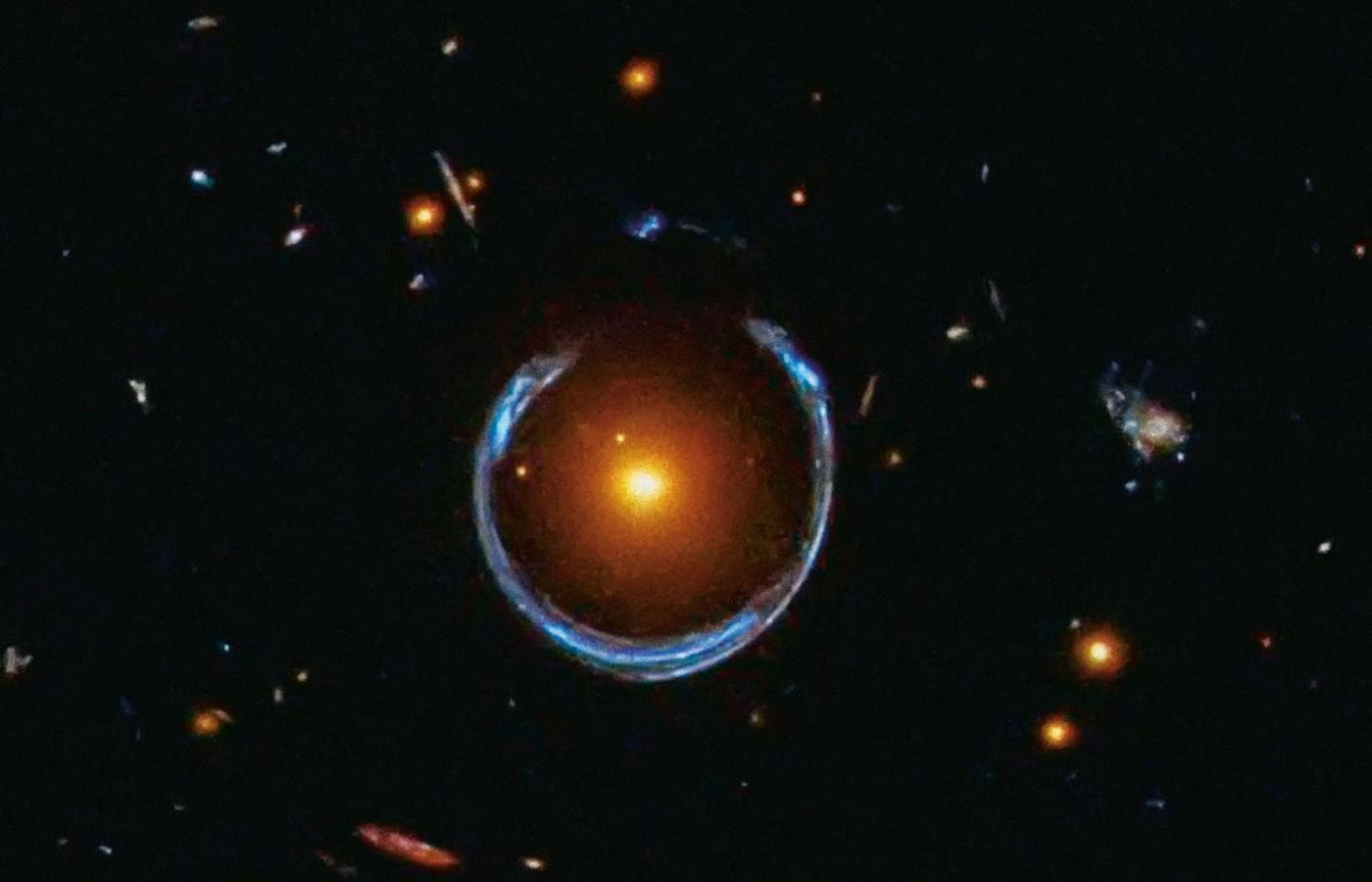 Przykład soczewkowania grawitacyjnego. Rolę soczewki pełni pole grawitacyjne żółtobrązowej galaktyki odległej od nas o 5 mld lat świetlnych. Niebieska podkowa jest utworzona ze zlanych ze sobą obrazów galaktyki leżącej w odległości 11 mld lat świetlnych.