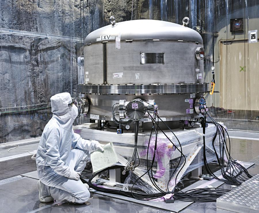 Odizolowanie od drgań. Technik klęczy obok górnej części wysokiego na 14 m systemu tłumienia drgań jednego z wypolerowanych szafirowych zwierciadeł detektora KAGRA. Takie układy są niezbędne, aby odizolować zwierciadła od szumu docierającego z zewnątrz i umożliwić zaobserwowanie subtelnego oddziaływania fali grawitacyjnej widocznego w postaci przemieszczenia zwierciadła o mniej niż tysięczną część średnicy protonu.