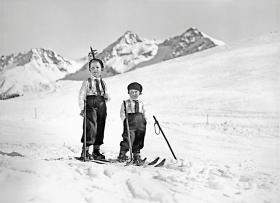 Dwoje dzieci na nartach na terenie narciarskim Arosy, w którym znajduje się popularny od dziesięcioleci ośrodek turystyczno-wypoczynkowy oraz uzdrowisko.