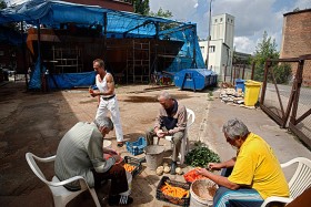 Mieszkańcy schroniska obierają warzywa przeznaczone dla punktu wydawania darmowych obiadów w centrum Warszawy. W tle trwa budowa statku.