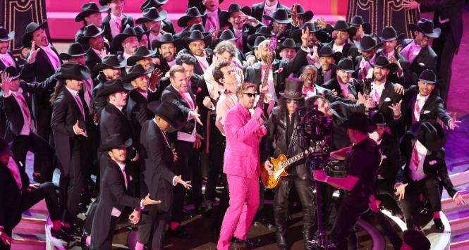 Ryan Gosling śpiewa piosenkę na gali oscarowej w otoczeniu Kenów. Obok gitarzysta Slash.