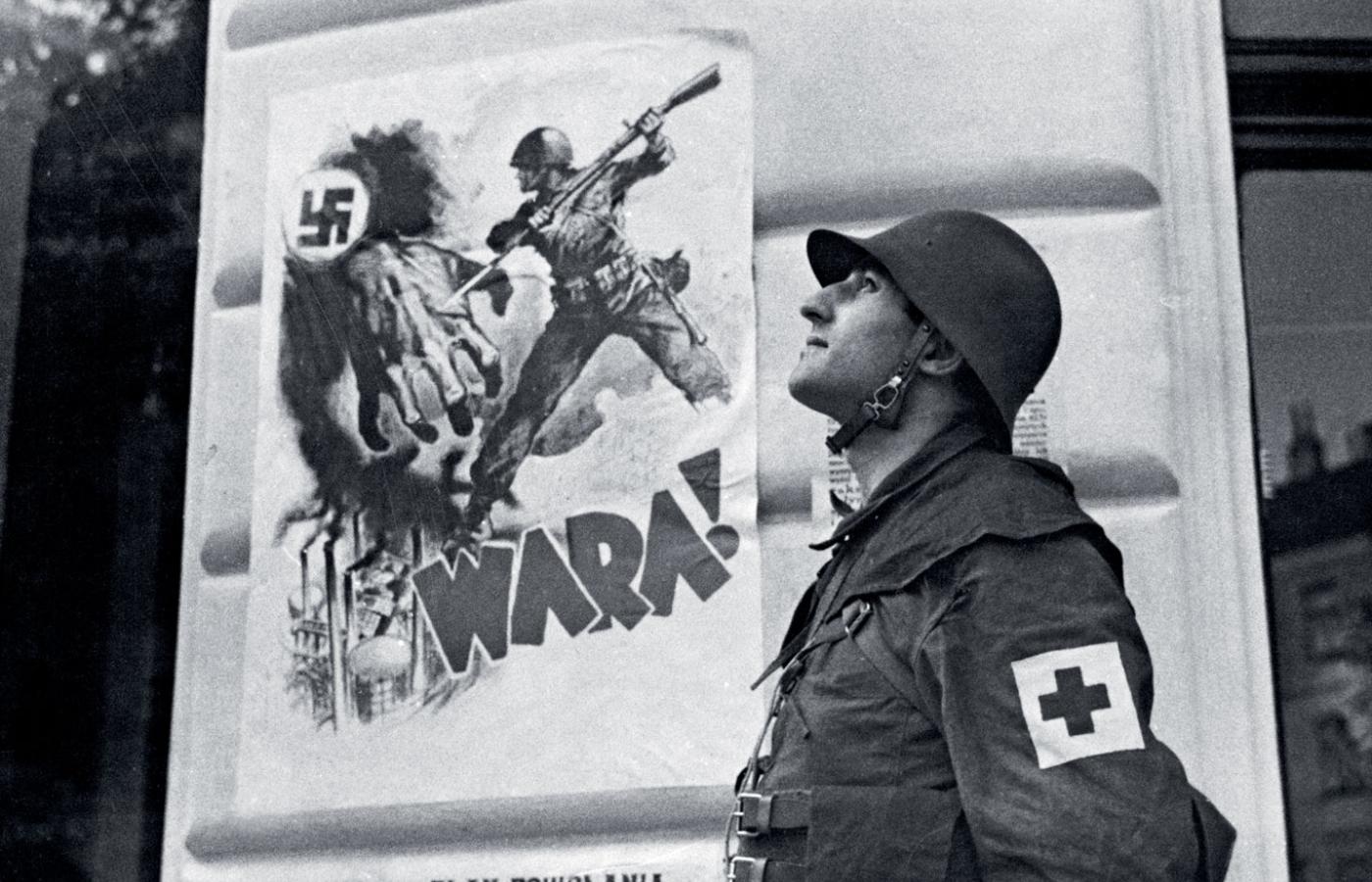 Członek drużyny ratowniczej PCK na tle plakatu antynazistowskiego, Warszawa, sierpień 1939 r.