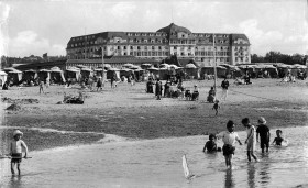 Plaża w nadmorskiej miejscowości Deauville, Francja około 1900 r., w tle hotel i pawilon wypoczynkowo-restauracyjny.